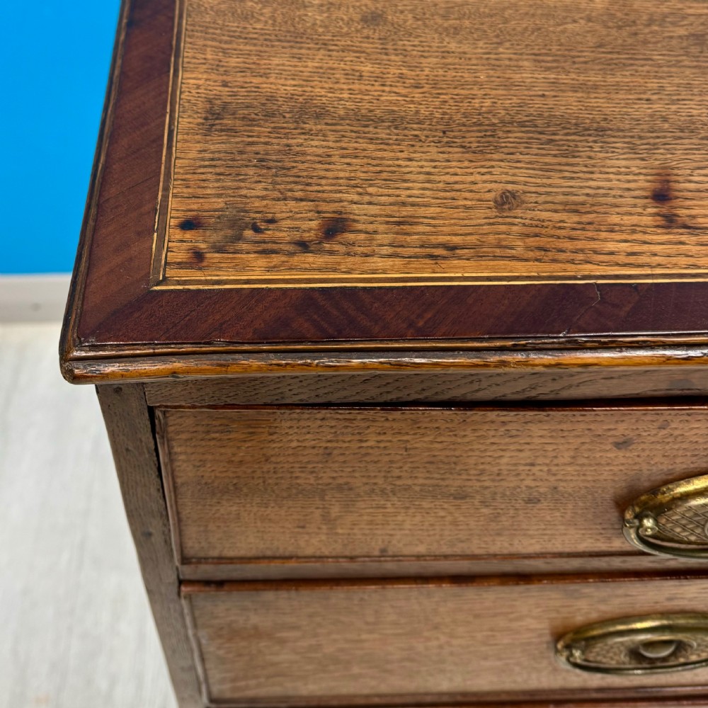 A Georgian oak chest of drawers featuring two short drawers over three long drawers with oval brass drop handles and bracket feet. View VIII