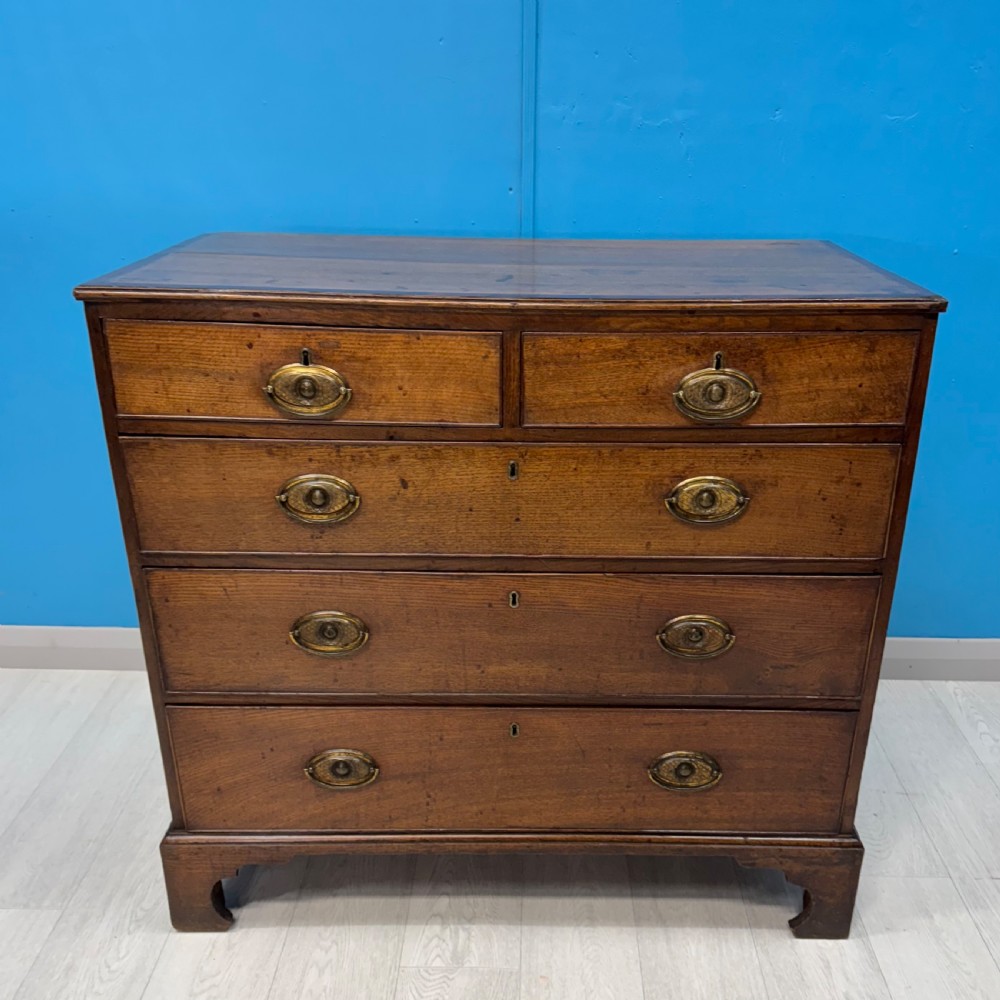 A Georgian oak chest of drawers featuring two short drawers over three long drawers with oval brass drop handles and bracket feet.