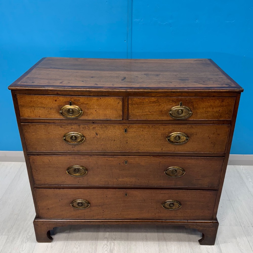 A Georgian oak chest of drawers featuring two short drawers over three long drawers with oval brass drop handles and bracket feet. View X