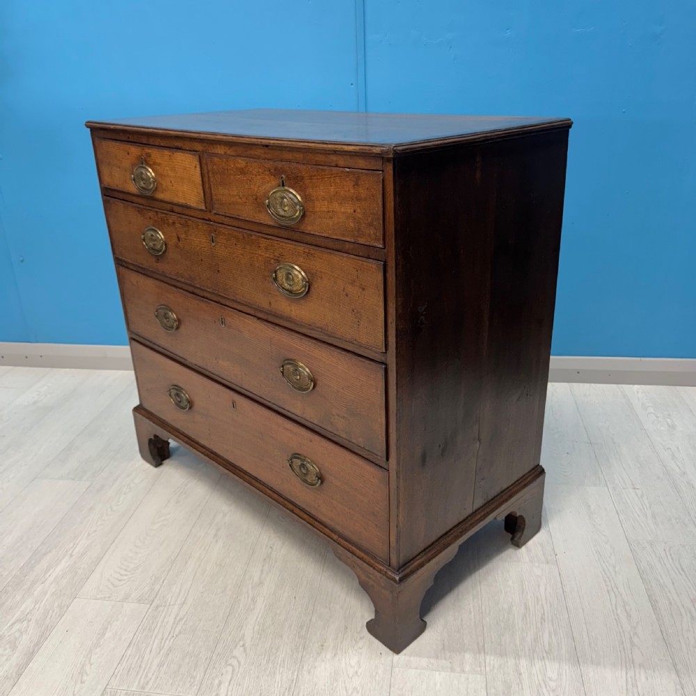 A Georgian oak chest of drawers featuring two short drawers over three long drawers with oval brass drop handles and bracket feet. View XI