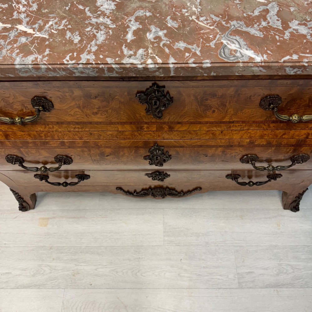 A French Louis XV style burr walnut commode featuring a curved bombee profile, three drawers with ornate brass handles, metal corner mounts, and a shaped marble top. View II