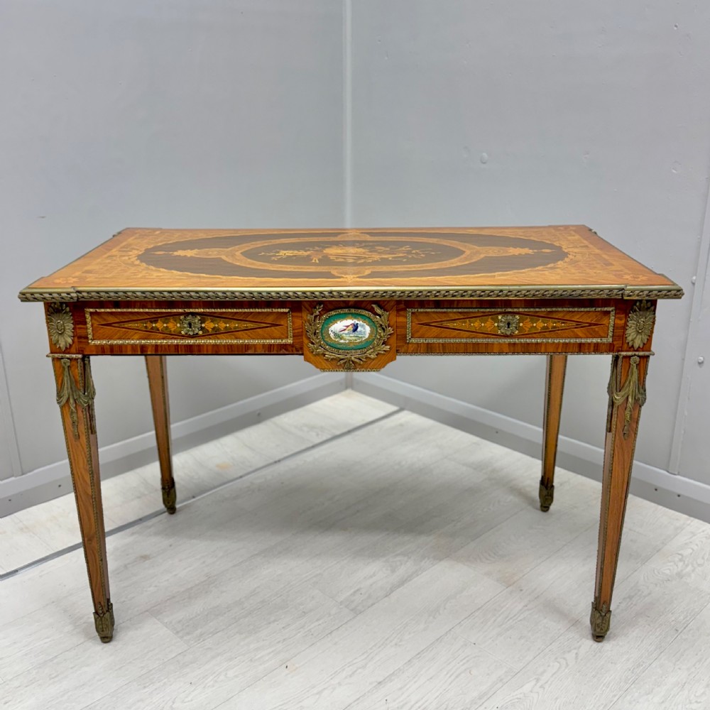A French Louis XVI style kingwood centre table featuring intricate floral marquetry, brass mounts, a central porcelain plaque, and tapered square legs.