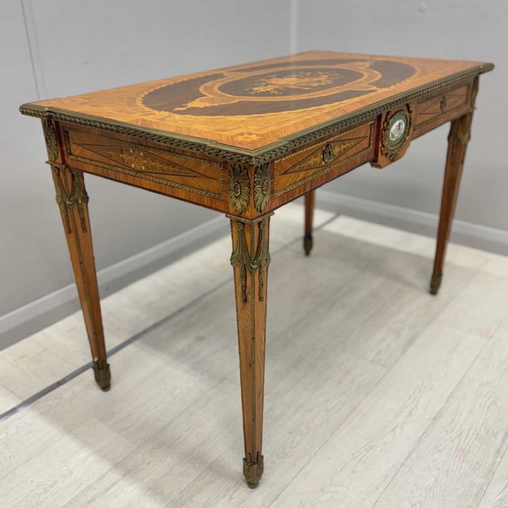 A French Louis XVI style kingwood centre table featuring intricate floral marquetry, brass mounts, a central porcelain plaque, and tapered square legs. View II