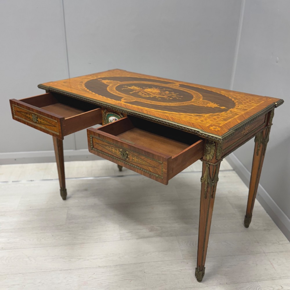 A French Louis XVI style kingwood centre table featuring intricate floral marquetry, brass mounts, a central porcelain plaque, and tapered square legs. View VI
