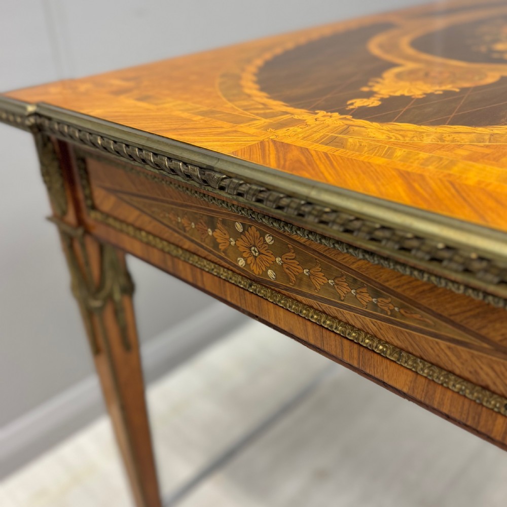A French Louis XVI style kingwood centre table featuring intricate floral marquetry, brass mounts, a central porcelain plaque, and tapered square legs. View IX