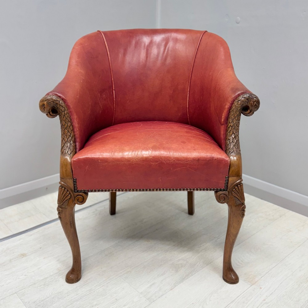 A red leather tub back armchair featuring carved mahogany cabriole legs, eagle head armrests, and brass studded trim.