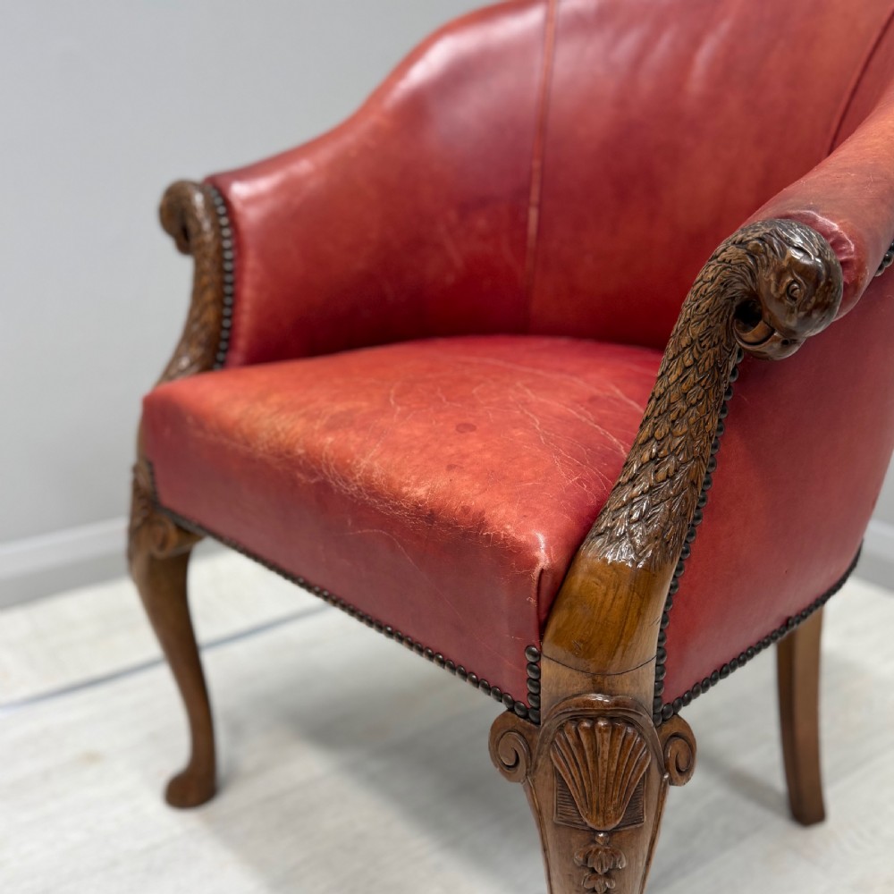A red leather tub back armchair featuring carved mahogany cabriole legs, eagle head armrests, and brass studded trim. View V