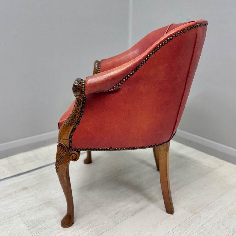 A red leather tub back armchair featuring carved mahogany cabriole legs, eagle head armrests, and brass studded trim. View VI