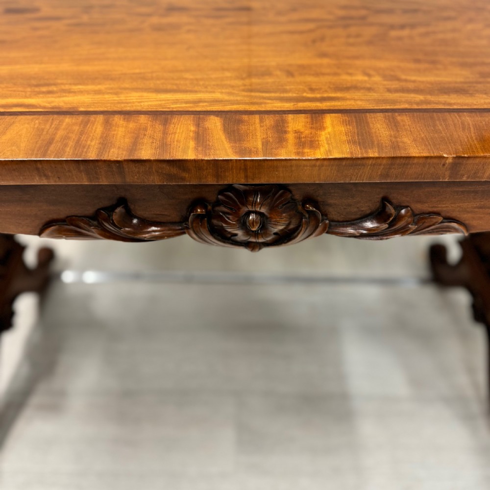 A 19th-century satinwood sofa table featuring a rectangular crossbanded top supported by carved trestle end supports and splayed legs on castors. View II