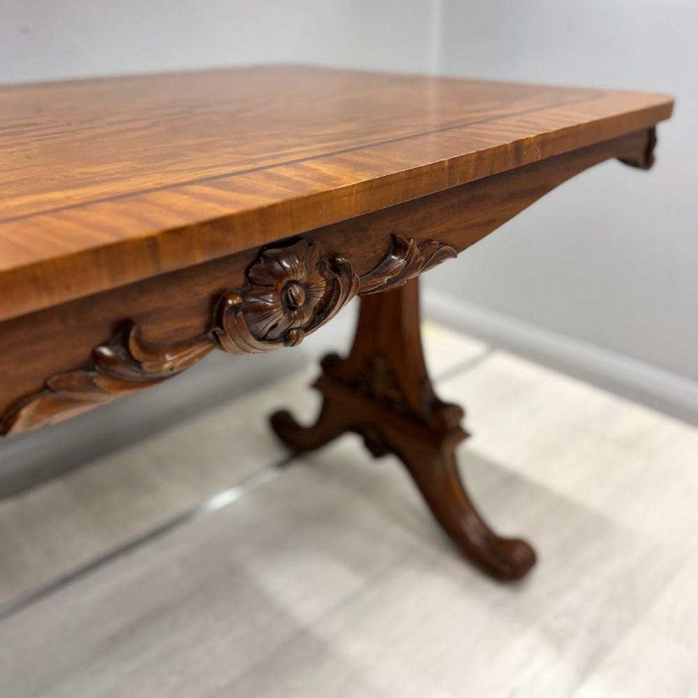 A 19th-century satinwood sofa table featuring a rectangular crossbanded top supported by carved trestle end supports and splayed legs on castors. View III