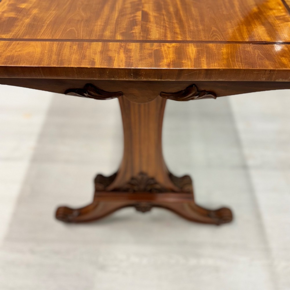 A 19th-century satinwood sofa table featuring a rectangular crossbanded top supported by carved trestle end supports and splayed legs on castors. View V