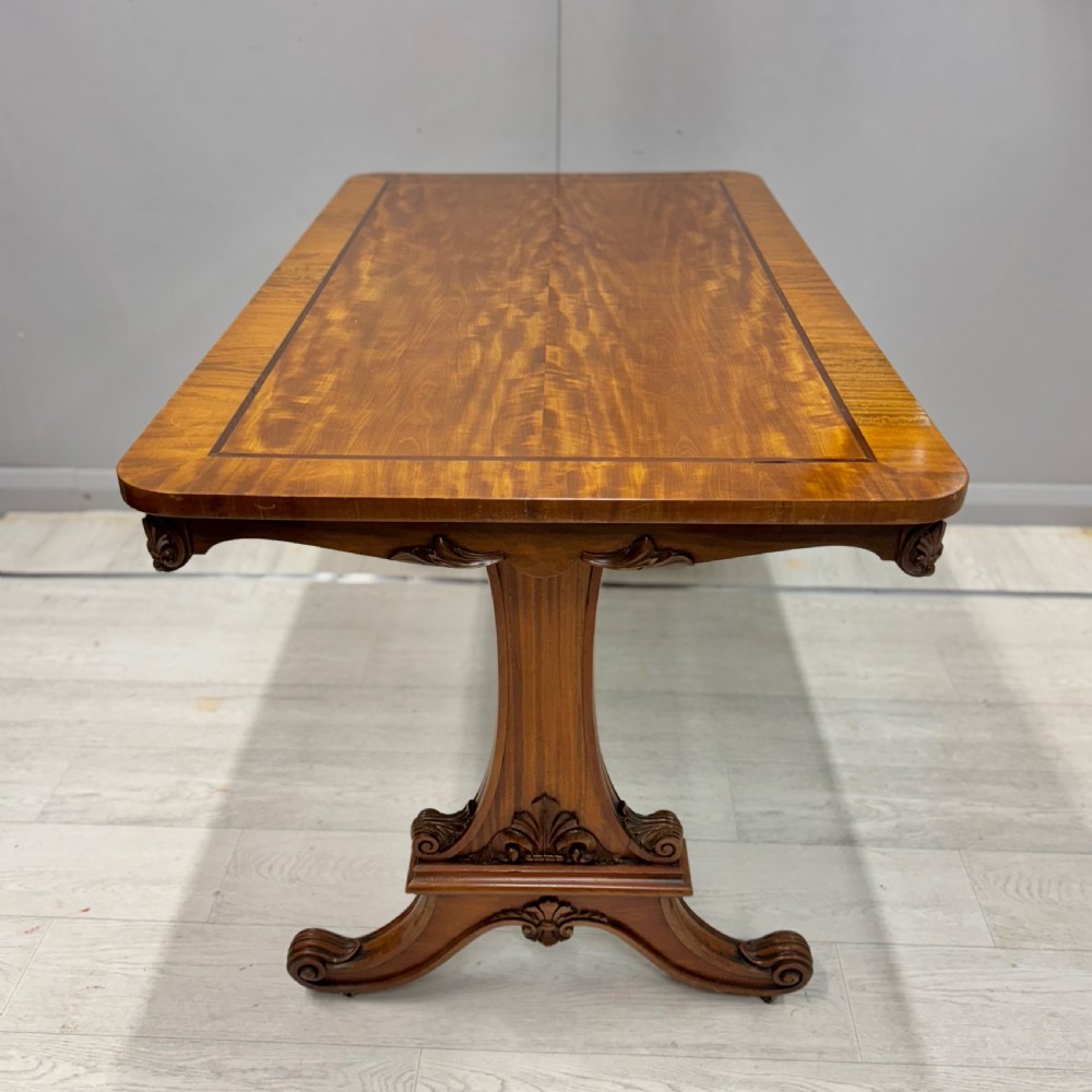 A 19th-century satinwood sofa table featuring a rectangular crossbanded top supported by carved trestle end supports and splayed legs on castors. View VII