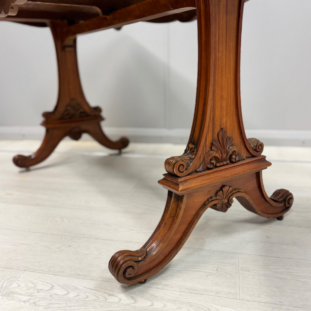 A 19th-century satinwood sofa table featuring a rectangular crossbanded top supported by carved trestle end supports and splayed legs on castors. View VIII