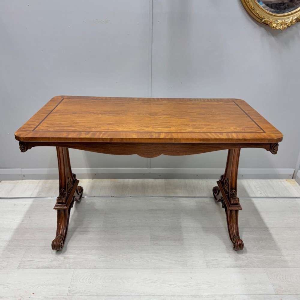 A 19th-century satinwood sofa table featuring a rectangular crossbanded top supported by carved trestle end supports and splayed legs on castors. View IX