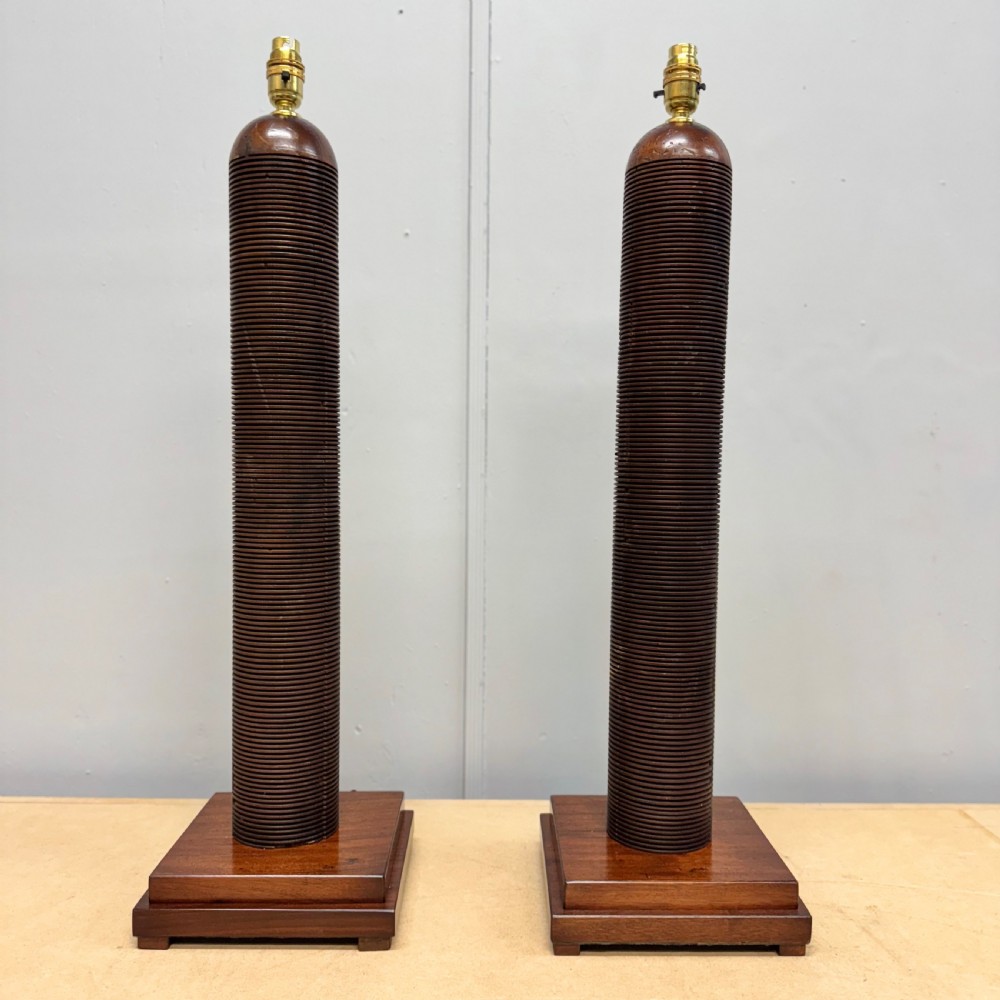 A matching pair of tall, dark wood table lamp bases featuring reeded cylindrical columns set on square plinths with brass bulb holders.