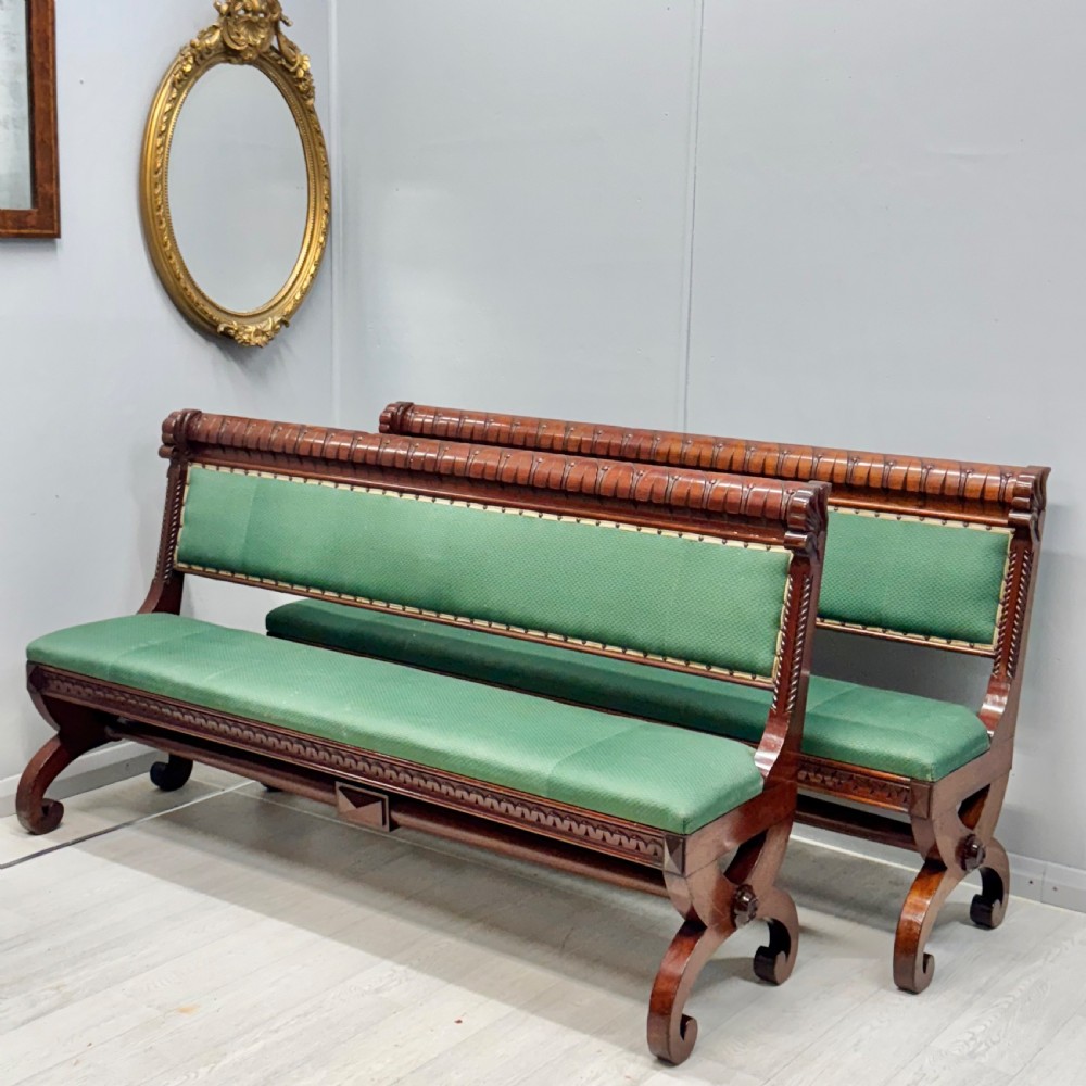 A pair of 19th-century carved mahogany benches featuring green upholstered seats and backrests supported by scrolled legs.