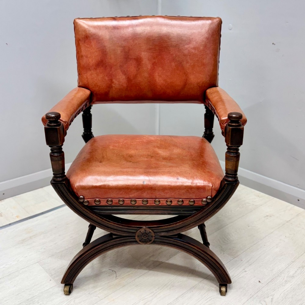 A French walnut X-frame armchair upholstered in tan leather with brass stud trim and carved wood accents.