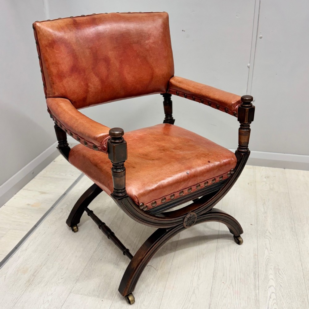 A French walnut X-frame armchair upholstered in tan leather with brass stud trim and carved wood accents. View II