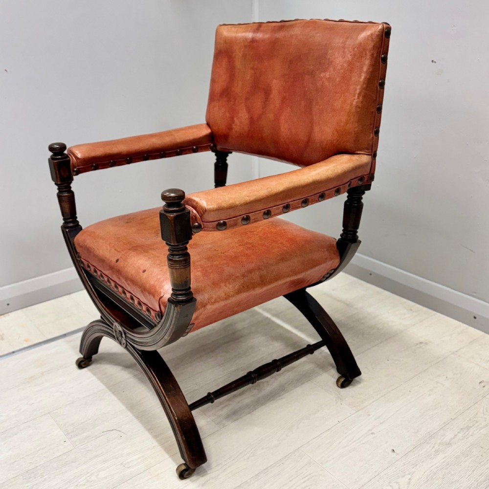A French walnut X-frame armchair upholstered in tan leather with brass stud trim and carved wood accents. View V