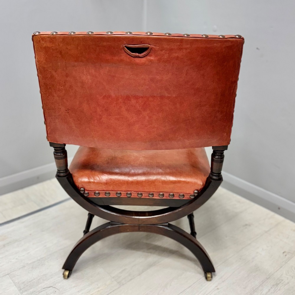 A French walnut X-frame armchair upholstered in tan leather with brass stud trim and carved wood accents. View VI