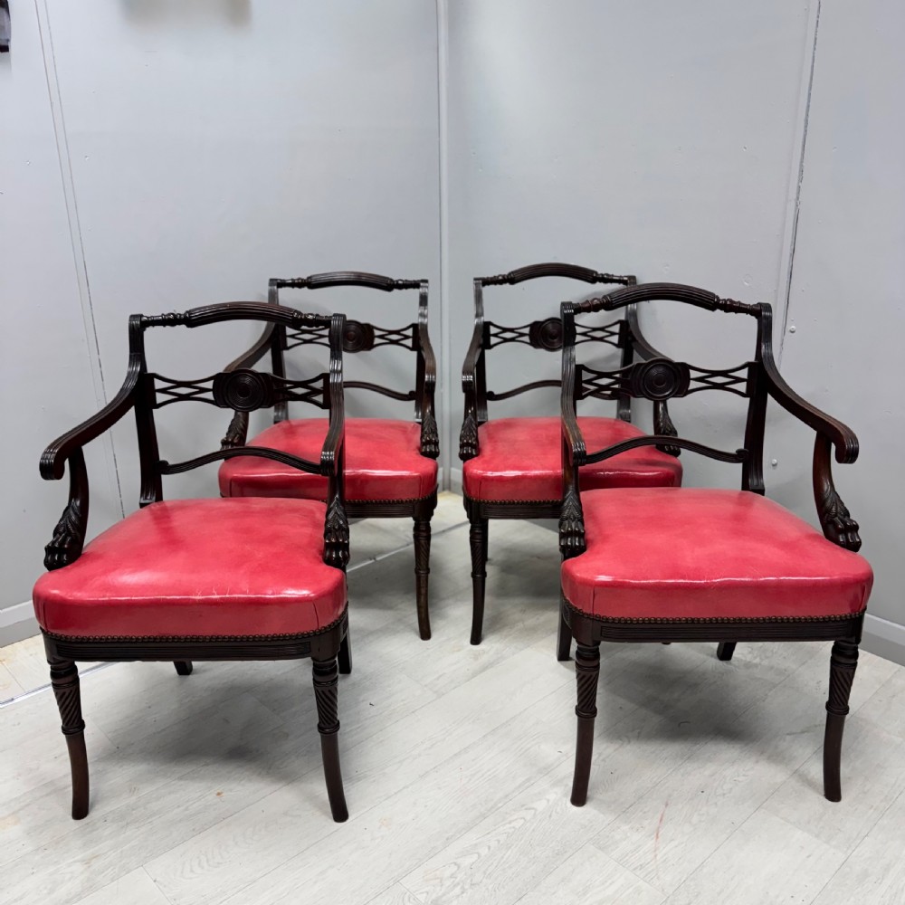 A set of four dark mahogany Regency style elbow chairs featuring carved rosettes, reeded arms, and red leather seats.