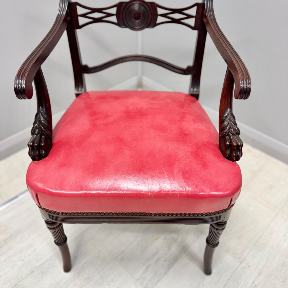 A set of four dark mahogany Regency style elbow chairs featuring carved rosettes, reeded arms, and red leather seats. View V