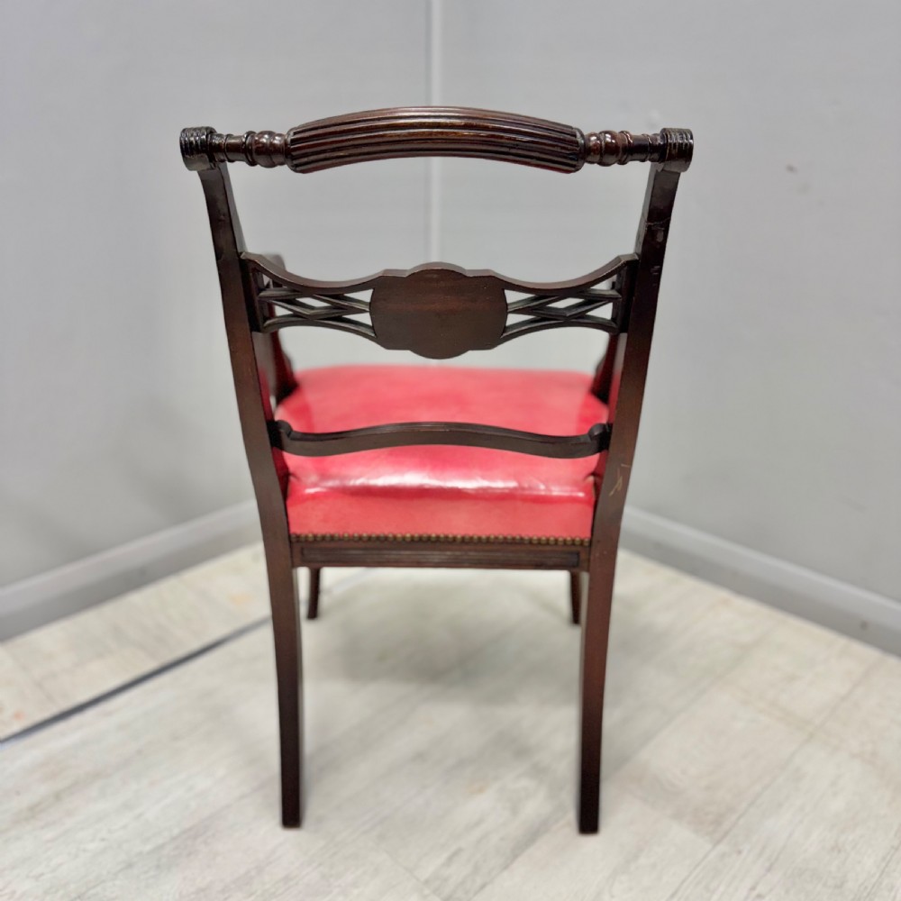 A set of four dark mahogany Regency style elbow chairs featuring carved rosettes, reeded arms, and red leather seats. View VIII