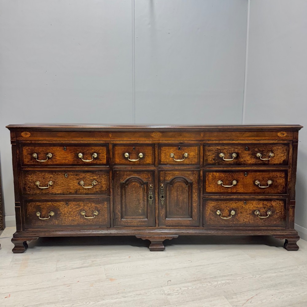 An 18th-century Georgian oak dresser base featuring inlaid fan motifs on the top frieze, multiple drawers with brass swan-neck handles, and twin central panelled cupboard doors.