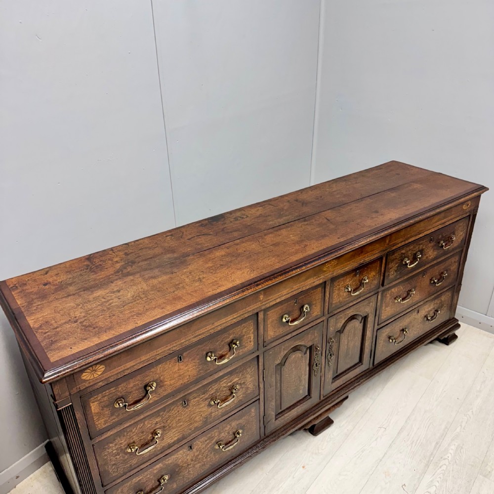 An 18th-century Georgian oak dresser base featuring inlaid fan motifs on the top frieze, multiple drawers with brass swan-neck handles, and twin central panelled cupboard doors. View II