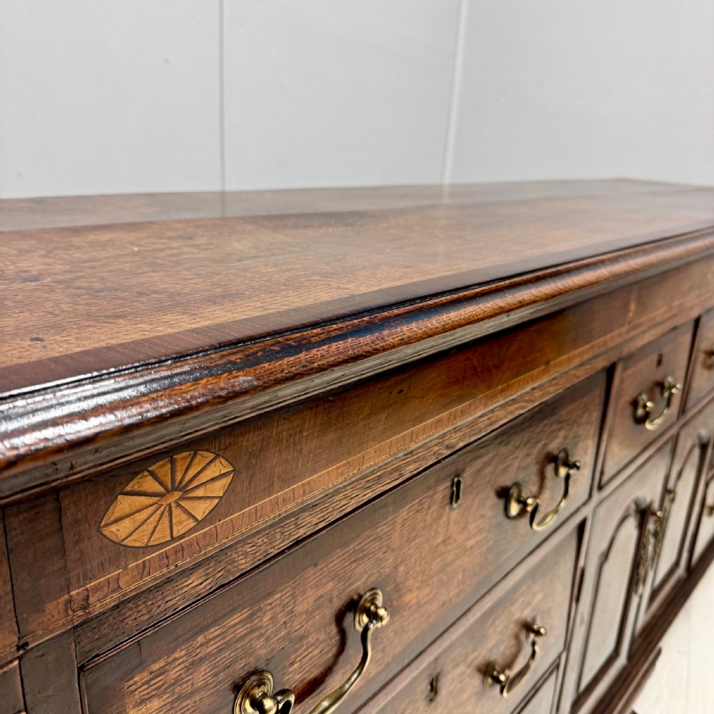 An 18th-century Georgian oak dresser base featuring inlaid fan motifs on the top frieze, multiple drawers with brass swan-neck handles, and twin central panelled cupboard doors. View III