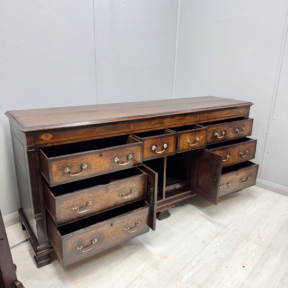 An 18th-century Georgian oak dresser base featuring inlaid fan motifs on the top frieze, multiple drawers with brass swan-neck handles, and twin central panelled cupboard doors. View V