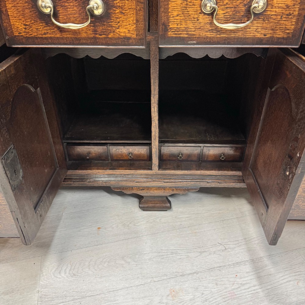 An 18th-century Georgian oak dresser base featuring inlaid fan motifs on the top frieze, multiple drawers with brass swan-neck handles, and twin central panelled cupboard doors. View VI