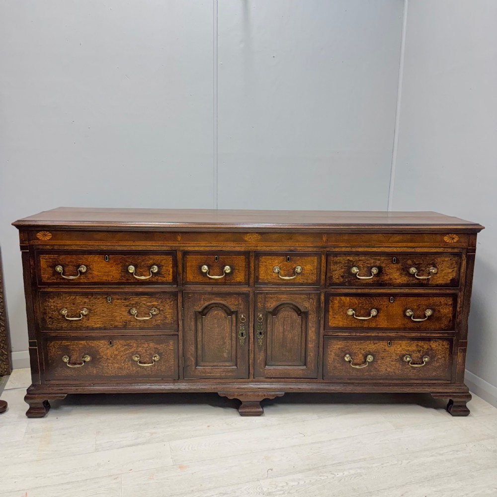 An 18th-century Georgian oak dresser base featuring inlaid fan motifs on the top frieze, multiple drawers with brass swan-neck handles, and twin central panelled cupboard doors. View VII