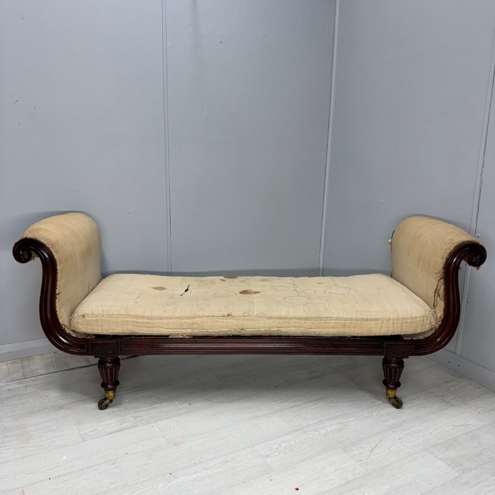 An antique Regency mahogany sofa frame featuring carved scroll arms, fluted turned legs on brass castors, and calico upholstery prepared for recovering. View II