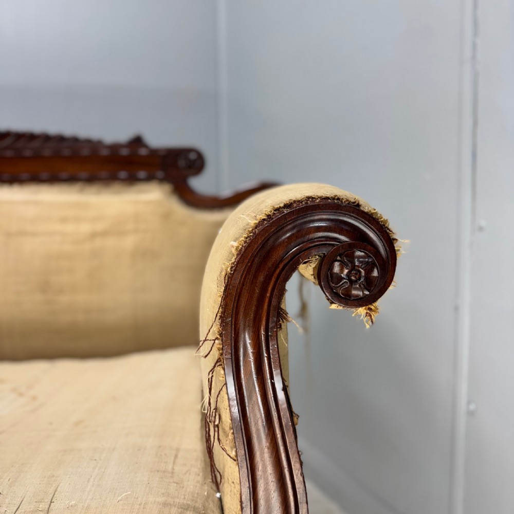 An antique Regency mahogany sofa frame featuring carved scroll arms, fluted turned legs on brass castors, and calico upholstery prepared for recovering. View V