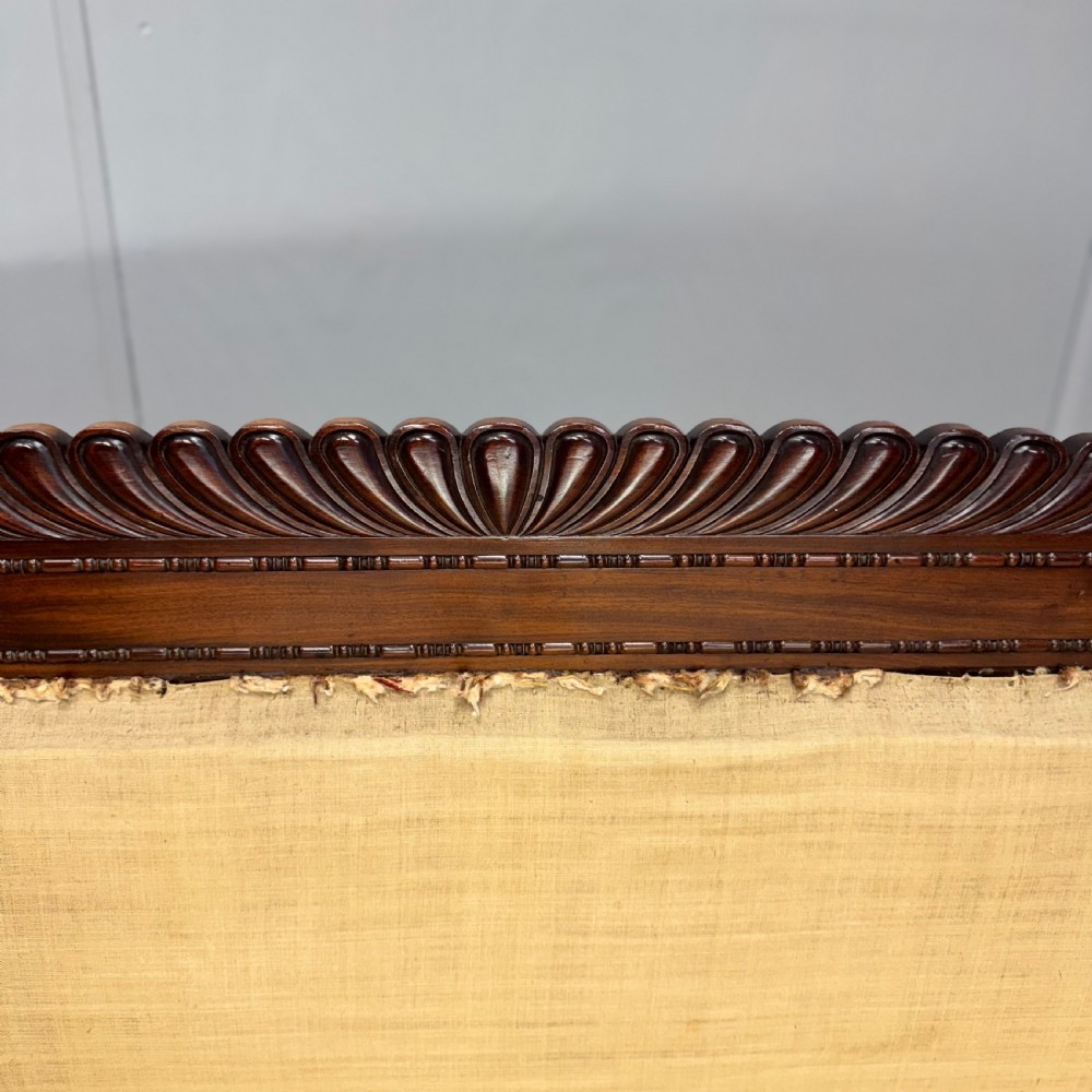 An antique Regency mahogany sofa frame featuring carved scroll arms, fluted turned legs on brass castors, and calico upholstery prepared for recovering. View VII