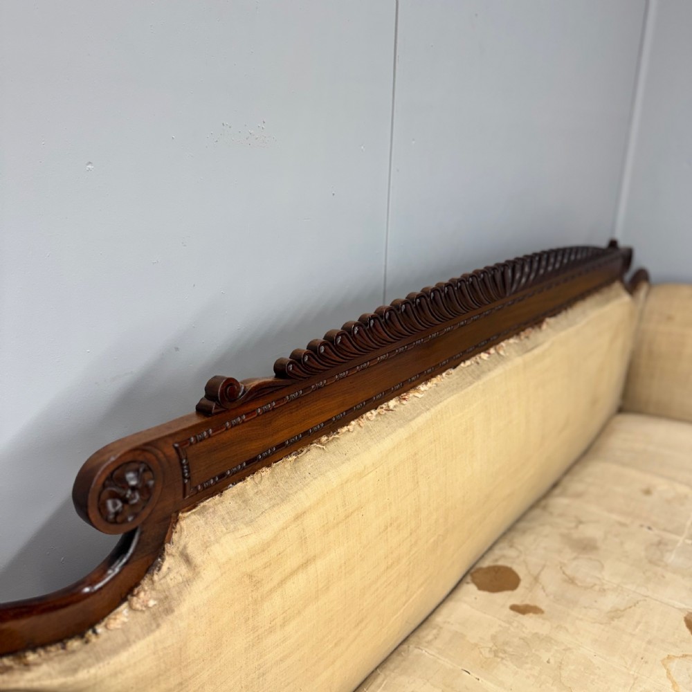 An antique Regency mahogany sofa frame featuring carved scroll arms, fluted turned legs on brass castors, and calico upholstery prepared for recovering. View VIII