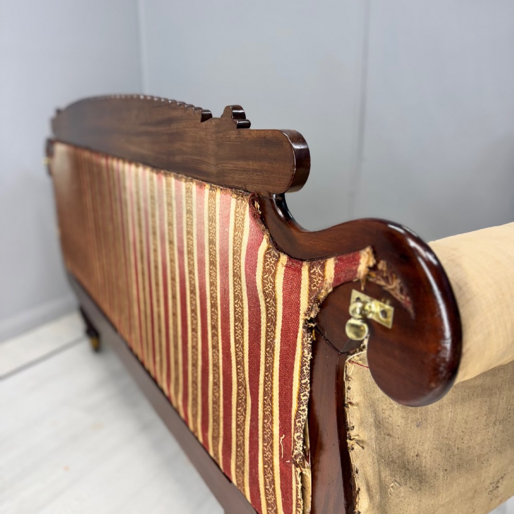 An antique Regency mahogany sofa frame featuring carved scroll arms, fluted turned legs on brass castors, and calico upholstery prepared for recovering. View XI