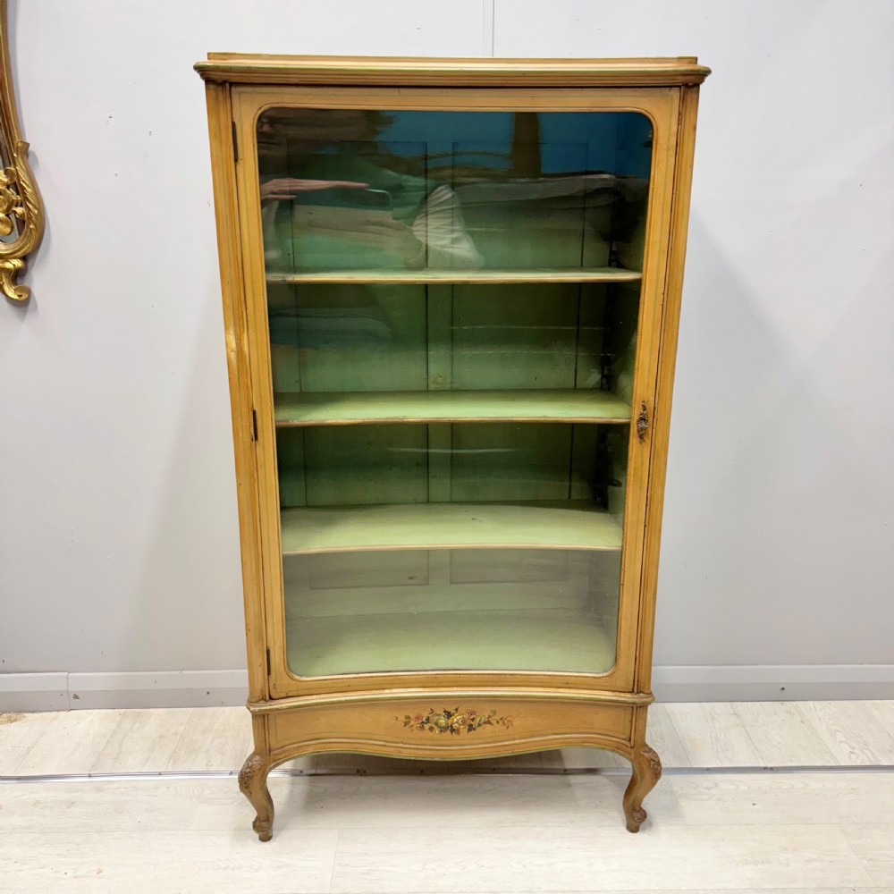 A freestanding cream painted bookcase featuring a single curved glass door, floral painted motifs, cabriole legs, and a sage green interior with adjustable shelves. View III