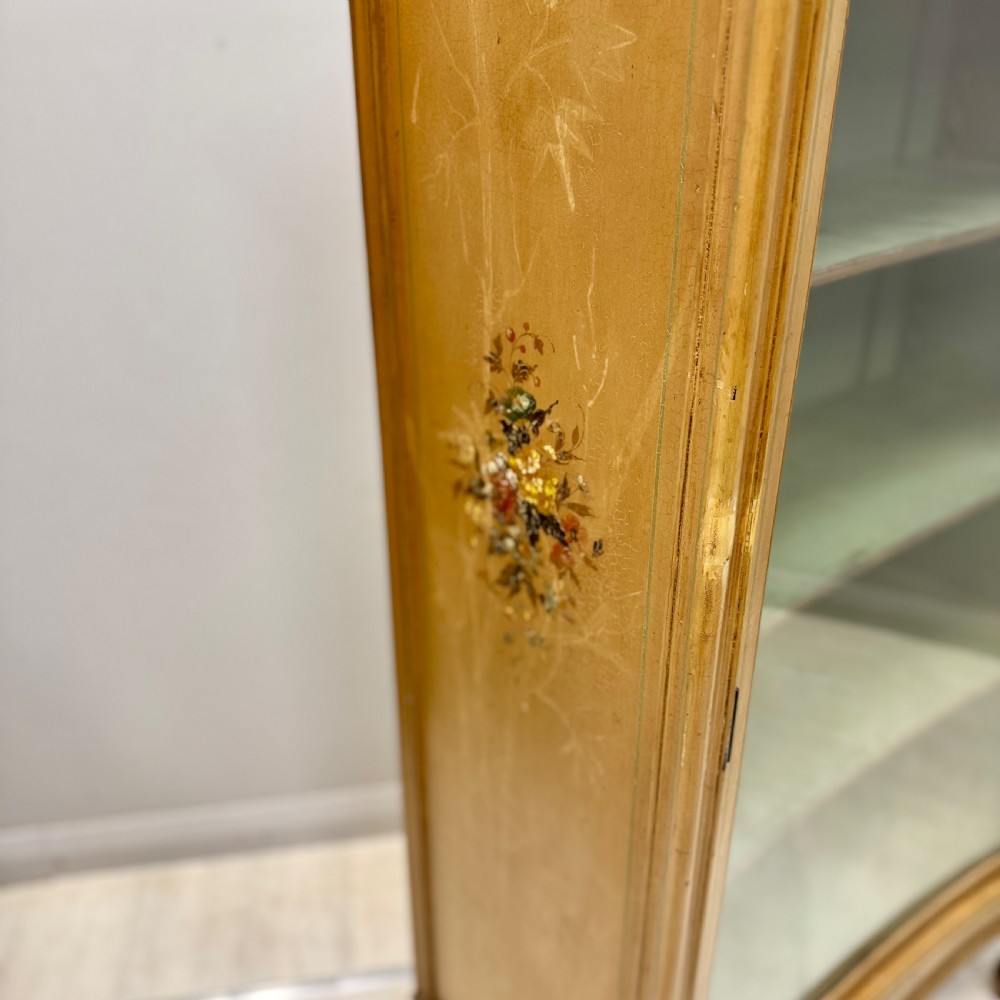 A freestanding cream painted bookcase featuring a single curved glass door, floral painted motifs, cabriole legs, and a sage green interior with adjustable shelves. View IX