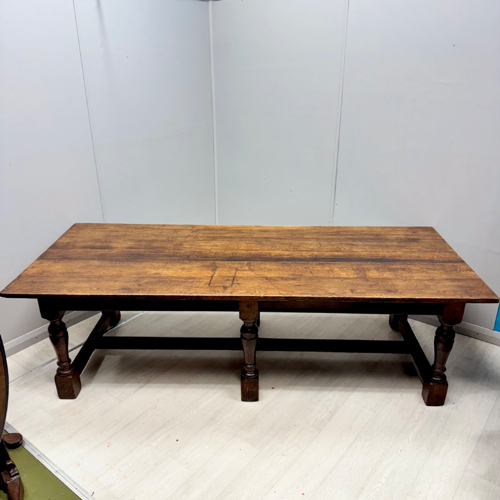 A large rectangular oak farmhouse dining table with a plank top, six turned legs, and a low H-stretcher base.