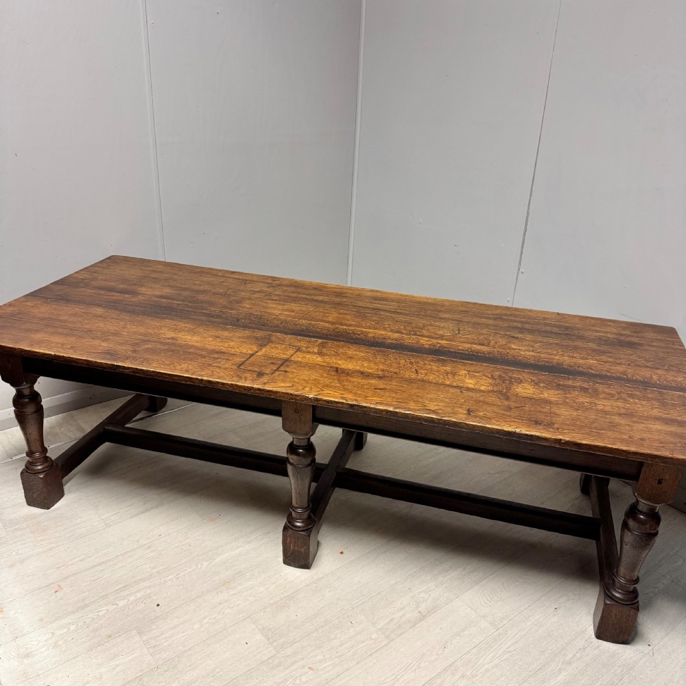 A large rectangular oak farmhouse dining table with a plank top, six turned legs, and a low H-stretcher base. View II