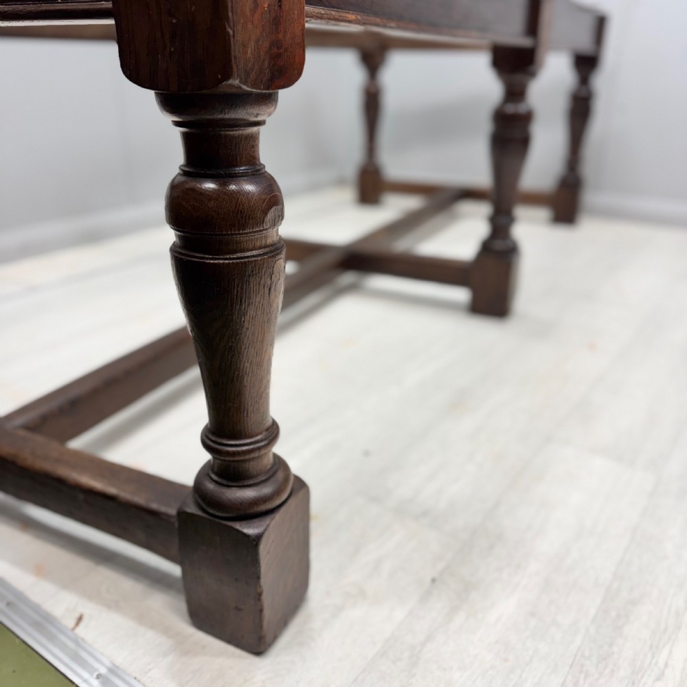 A large rectangular oak farmhouse dining table with a plank top, six turned legs, and a low H-stretcher base. View III