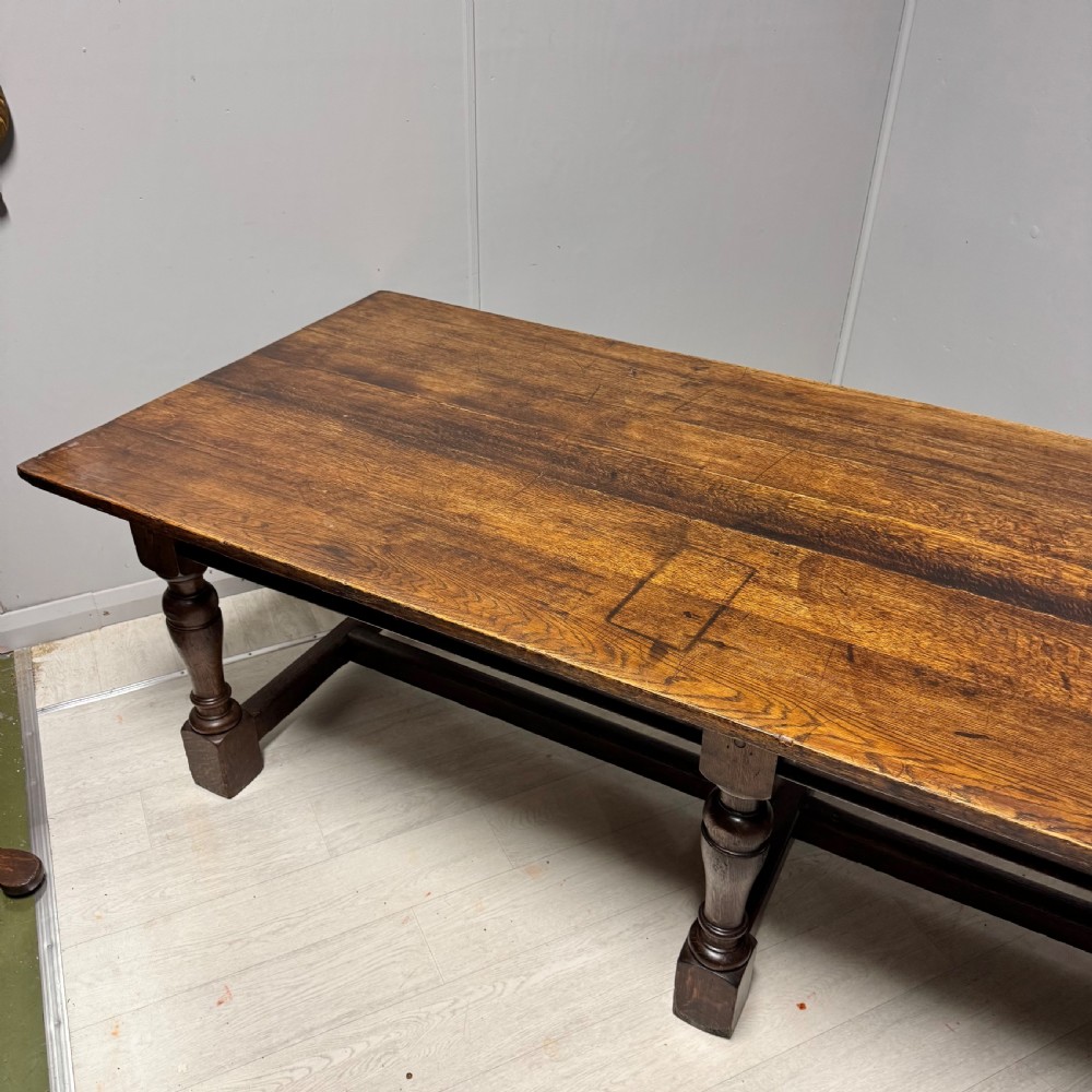A large rectangular oak farmhouse dining table with a plank top, six turned legs, and a low H-stretcher base. View V