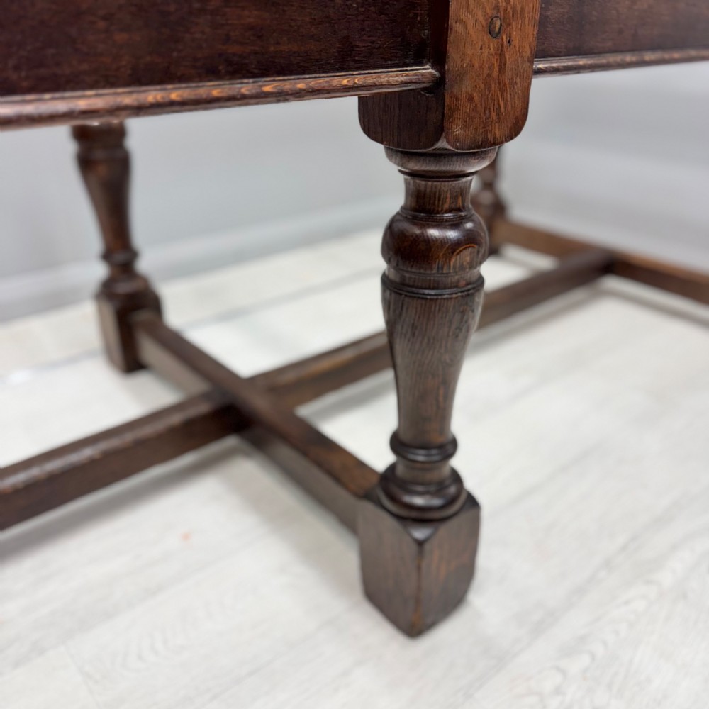 A large rectangular oak farmhouse dining table with a plank top, six turned legs, and a low H-stretcher base. View VI