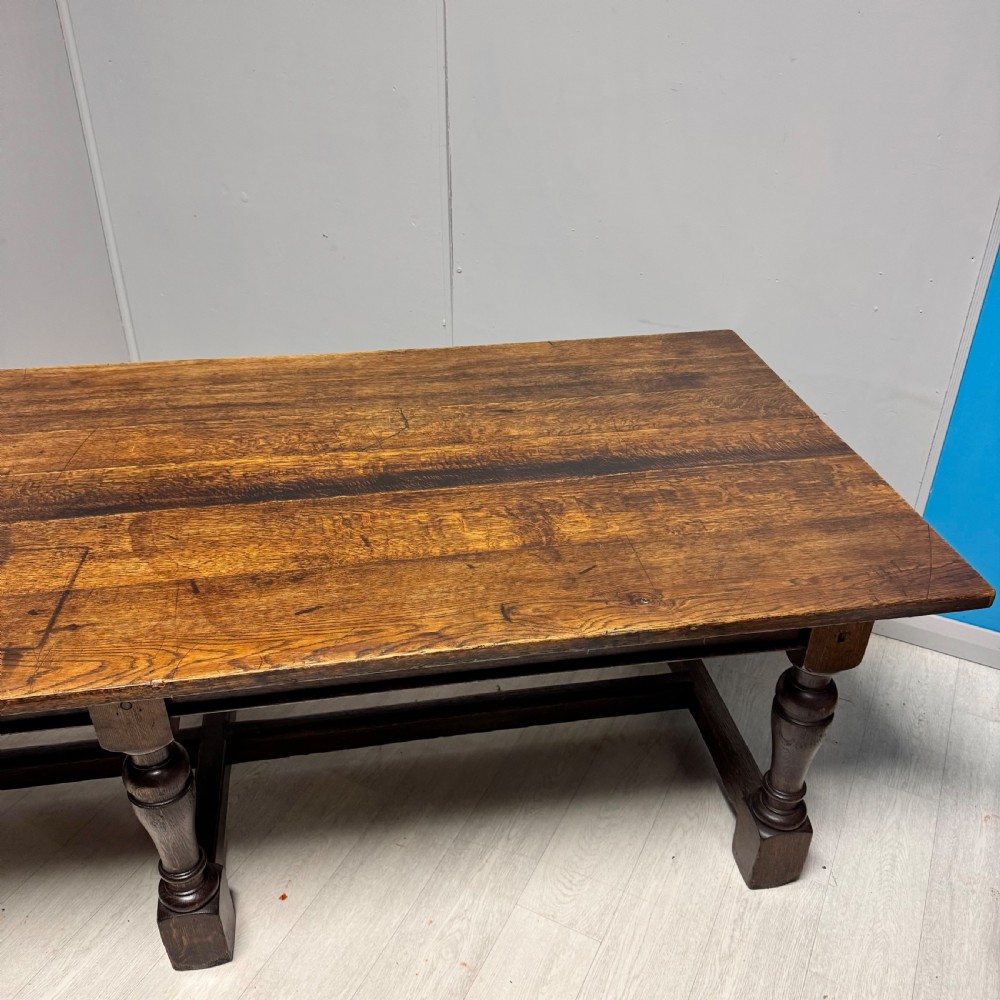 A large rectangular oak farmhouse dining table with a plank top, six turned legs, and a low H-stretcher base. View VII
