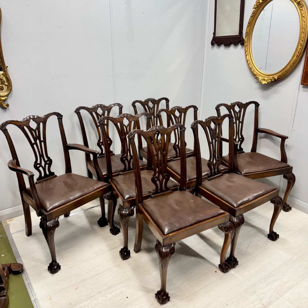 A set of eight Georgian style mahogany dining chairs featuring pierced back splats, brown leather seats, and cabriole legs ending in ball and claw feet.