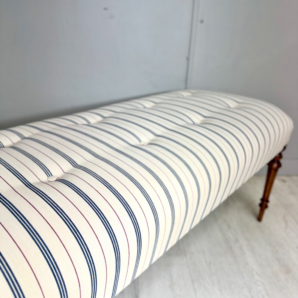 An elongated antique footstool featuring button-tufted ticking stripe upholstery and dark turned wooden legs. View II