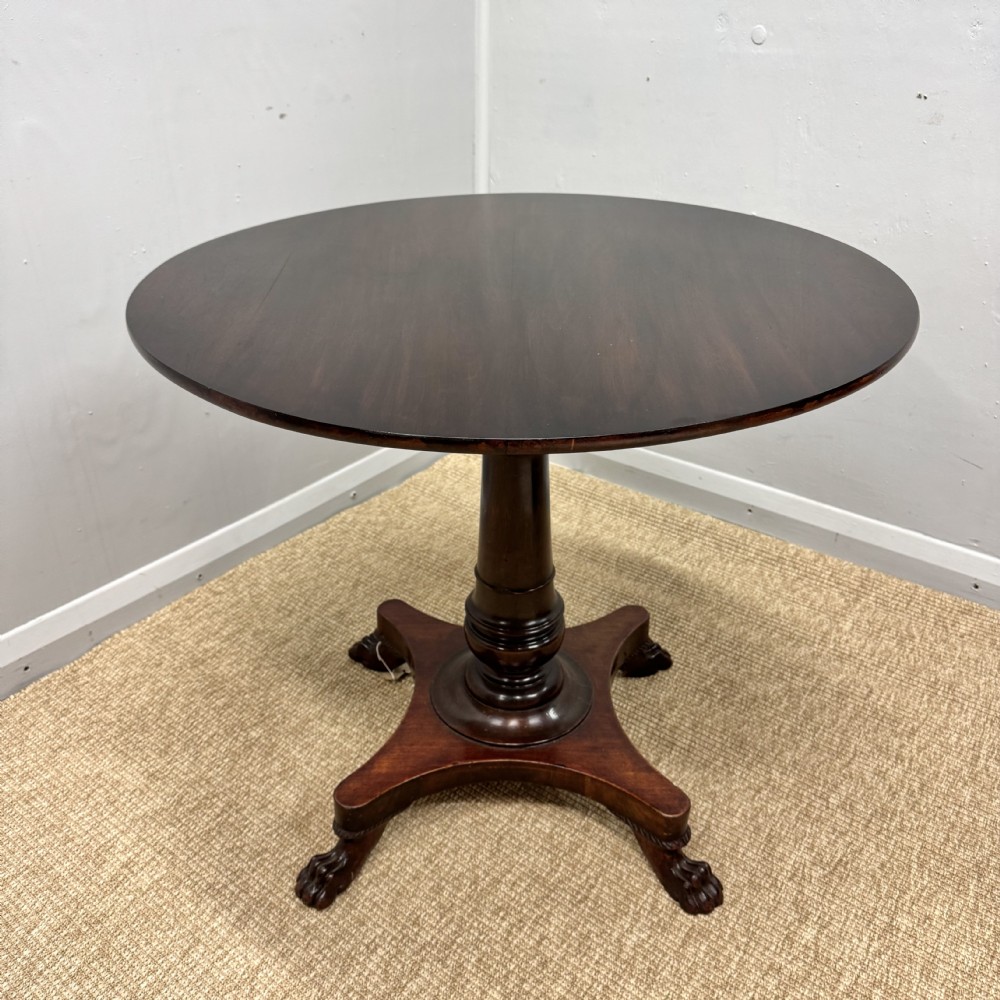 A round dark mahogany pedestal side table featuring a turned central column and a four-legged base with carved lion paw feet.