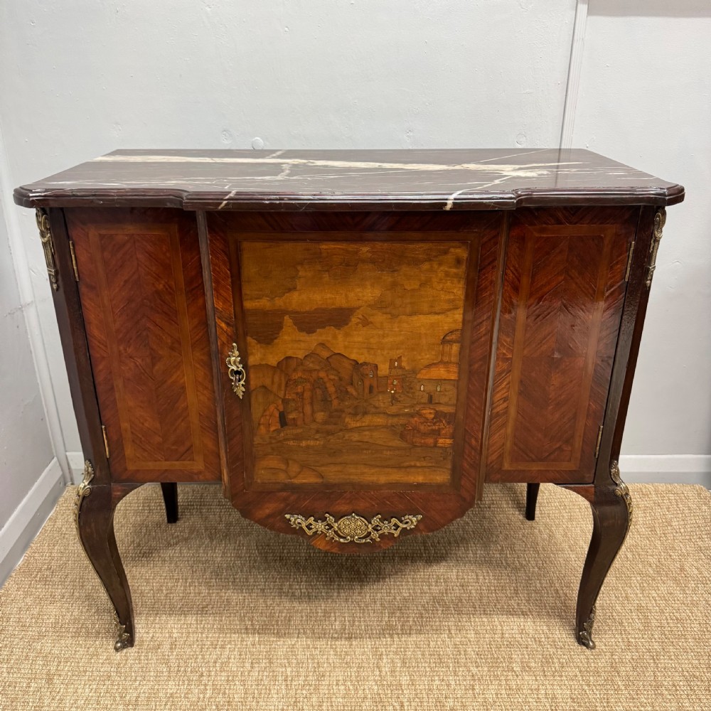 An early nineteenth-century French style marquetry commode cabinet with a marble top, cabriole legs, central inlaid architectural landscape scene, and decorative brass mounts. View IX